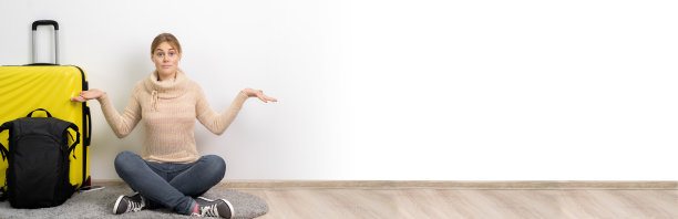 在白色背景上，穿着休闲服装、背着旅行箱和背包的女游客以怀疑的姿态耸着肩膀。境外旅客旅行。飞行旅程图片下载