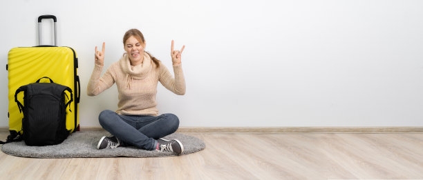 穿着毛衣的旅行箱的女旅行者准备去旅行，手指显示摇滚符号，好像在听最喜欢的音乐。旅客周末出国旅游度假。图片下载