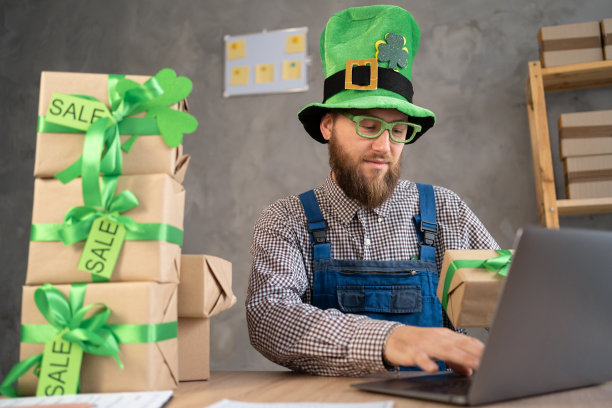 开始成功的小企业主在妖精帽子，工作在家与笔记本电脑和网上购买购物订单和盒子包装在桌子上。圣帕特里克节大减价图片下载