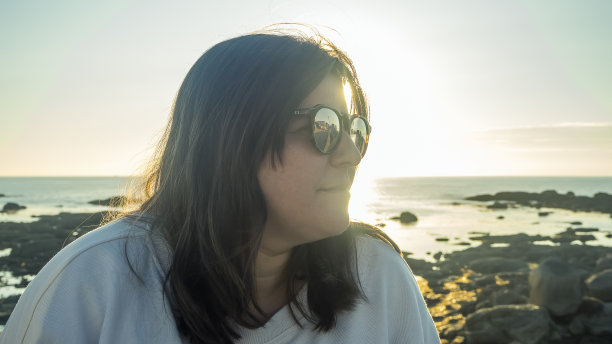 这张照片是在海边日落时戴着墨镜的白人女性的侧面特写图片下载