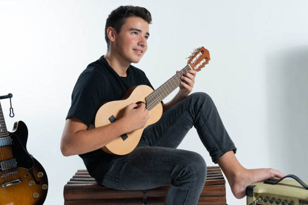 一个西班牙白人少年坐在白色背景前弹奏四弦琴图片下载
