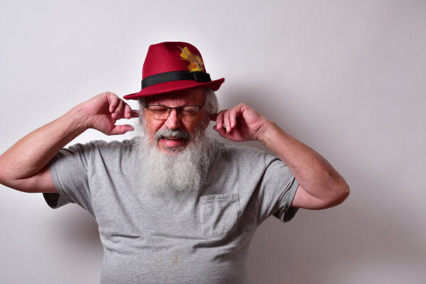 一个穿着灰色衬衫和红色软呢帽的老男人用手指堵住耳朵图片下载