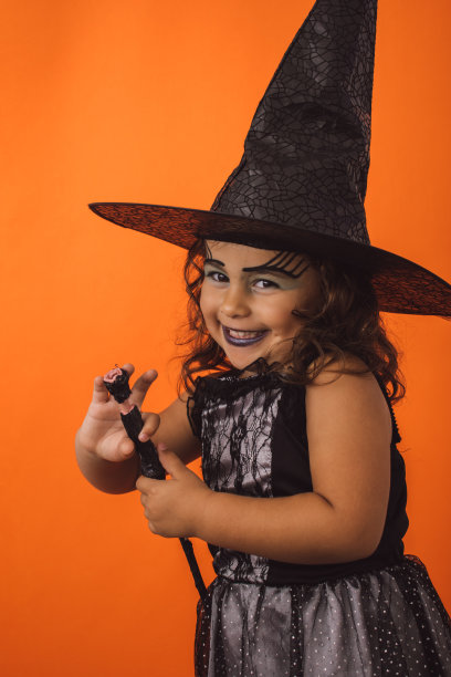 垂直拍摄一个穿着女巫服装的女孩子，橙色背景上有一根魔杖图片下载