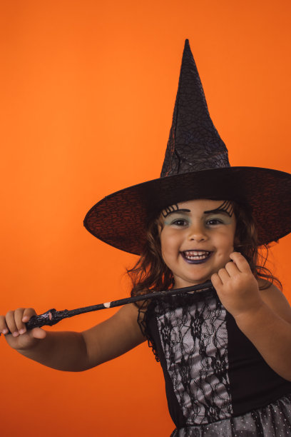 垂直拍摄一个穿着女巫服装的女孩子，橙色背景上有一根魔杖图片下载