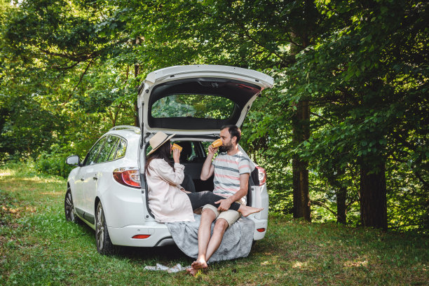 快乐的年轻夫妇在露营公路旅行坐在汽车后备箱喝咖啡。图片下载