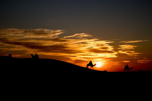 在橙色的夕阳下，人们和骆驼一起走过沙漠中的一座小山图片下载