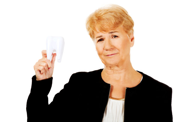 一名年长的白人妇女拿着一颗牙齿，脸上带着忧虑的表情图片下载