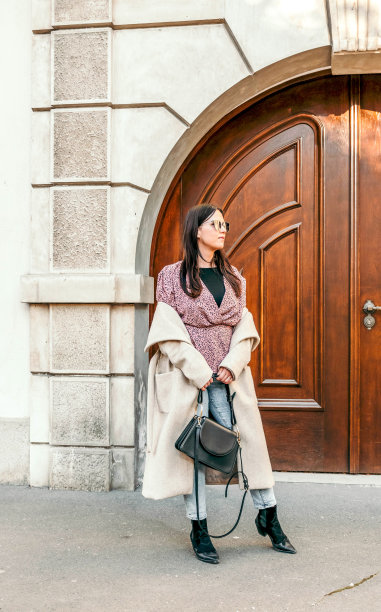 一个穿着外套、戴着墨镜的美丽白人女子在外面摆姿势的垂直镜头图片下载