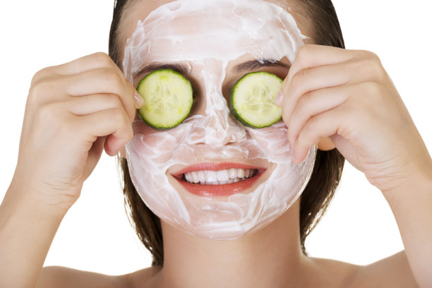 美丽的女人用面膜把黄瓜片放在她的眼睛图片下载