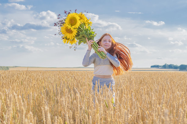 快乐的小女孩，红头发，捧着野花，跑过金色的麦田图片下载
