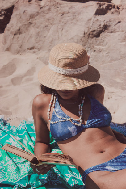 年轻的女性躺在沙滩上看书图片下载
