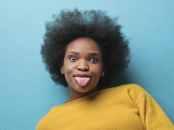 一个年轻快乐的黑人妇女的肖像与短卷发伸出她的舌头图片下载