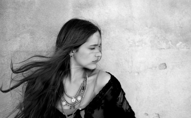 一个穿着黑色连衣裙和项链摆姿势的女人的美丽灰度视图图片下载
