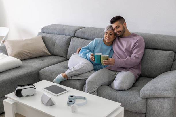 一对快乐的年轻西班牙夫妇坐在沙发上喝咖啡，享受时光图片下载