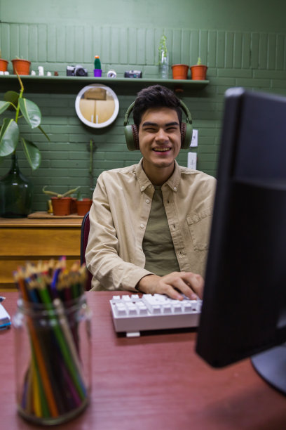 一个带着耳机微笑的西班牙男性坐在电脑前的一张桌子旁图片下载