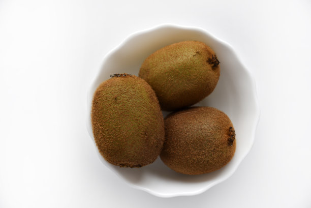 白色盘子里有三个绿色的猕猴桃。白色背景的猕猴桃。图片下载