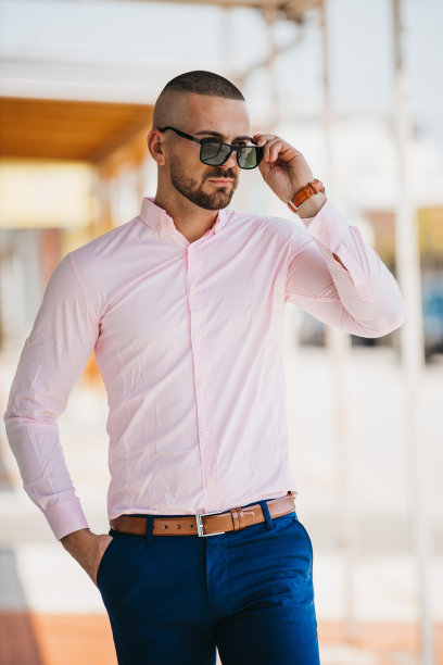 酷帅的白人男子穿着优雅的浅粉色衬衫和太阳镜在户外摆姿势图片下载