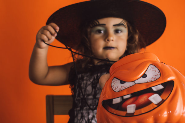 白人女孩子穿着女巫服装，手里拿着一个南瓜，背景是橙色的图片下载