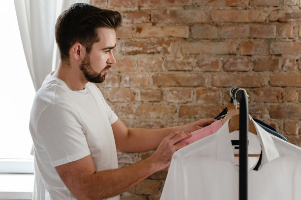 一名男子正在衣柜的衣架上浏览他的各种衬衫图片下载