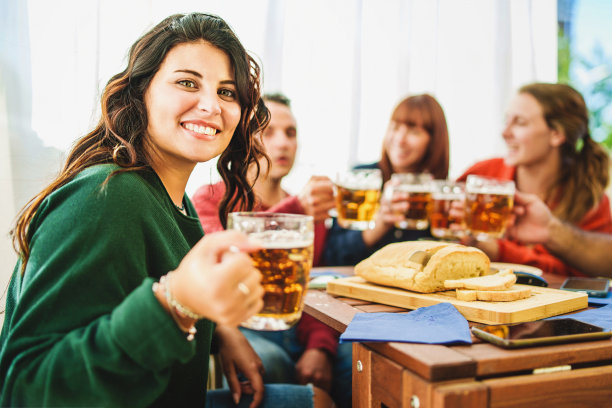 年轻女子看着镜头与啤酒和朋友庆祝图片下载