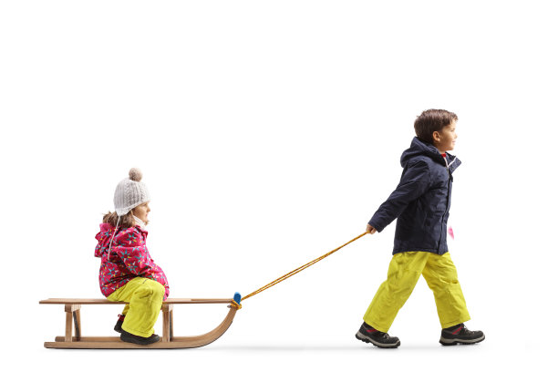 一个男孩拉着一个女孩的全长侧面照片，白色背景上孤立着一个木制雪橇图片下载