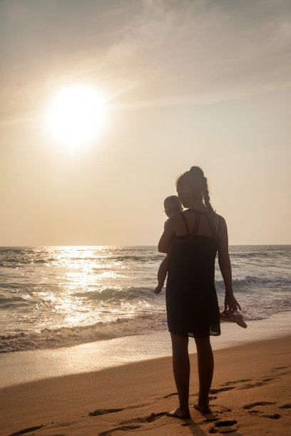 剪影妈妈与婴儿在怀里站在热带海滩在海上的背景。女人带着小孩在夏天享受假期。母亲的概念和与孩子的娱乐。复制文本空格图片下载