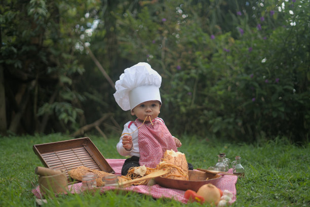白人小孩，嘴里含着意大利面，穿着厨师制服，站在草地上图片下载