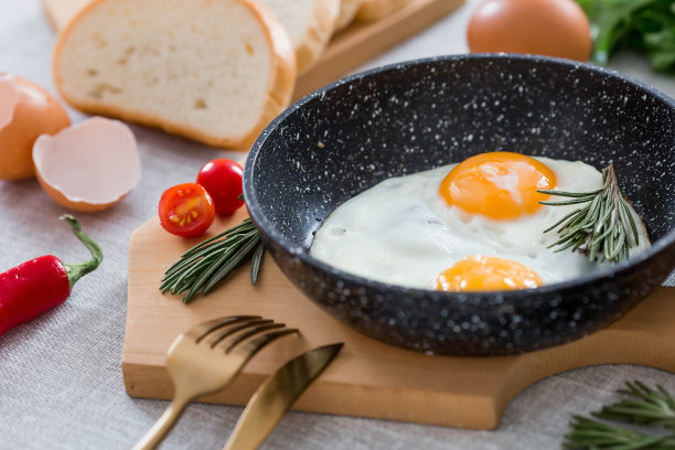 在平底锅里煎蛋，配上迷迭香、面包、鸡蛋和蔬菜沙拉，铺在亚麻桌布上。早餐，午餐和晚餐。视图是软的，选择性聚焦。乡村风格。图片下载