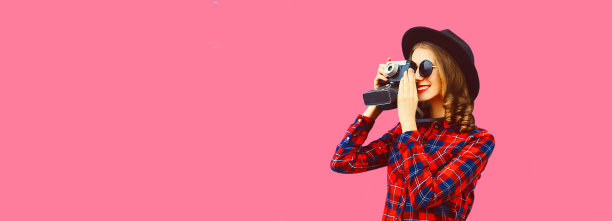 幸福微笑的年轻女子摄影师的肖像与电影相机在粉红色的背景，空白复制空间的广告文字图片下载
