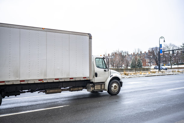 在新英格兰，白色的一天驾驶室中间钻井半挂车与长箱拖车运输货物到当地客户行驶在湿滑的冬季城市道路上图片下载