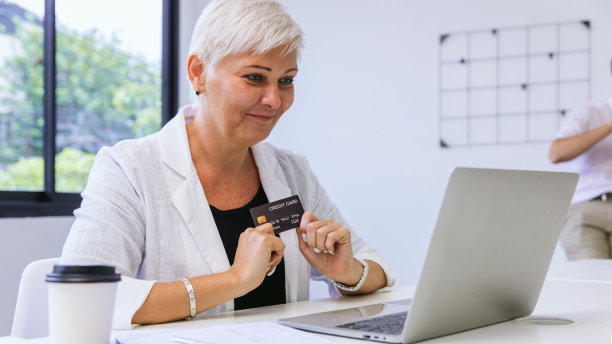 手持信用卡和笔记本电脑在家网购的老年女性消费者。女人网上航运与信用卡在手。女性使用笔记本电脑技术支付网上信用卡购物图片下载