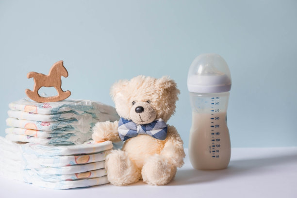 木制玩具，一只戴领结的熊，一堆尿布，一个奶瓶和婴儿用品放在换尿布的桌子上。文本空格。图片下载