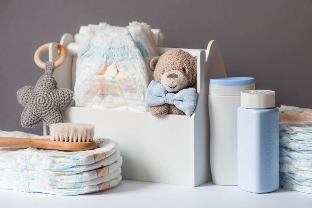 木制玩具、戴领结的熊、一堆尿布、没有标签的奶瓶和婴儿用品放在换尿布的桌子上。文本空格。图片下载