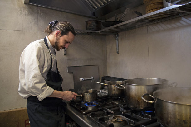 年轻的厨师在餐厅厨房靠近炉子的地方烹饪美味的食物图片下载