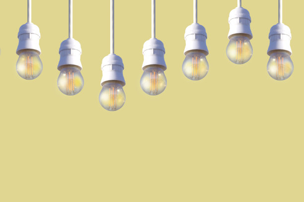 米色背景上，一排白色电灯泡挂在电线上。图片下载