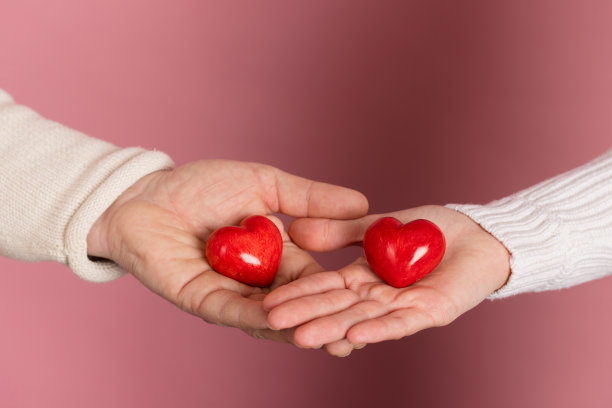 特写:粉色背景上的手握着心形，情人节的概念图片下载