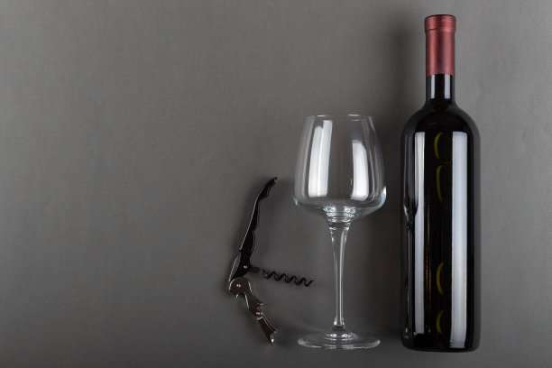 灰色背景上的红色酒瓶，开塞钻和空酒杯。酒精饮料。酿酒的概念。图片下载