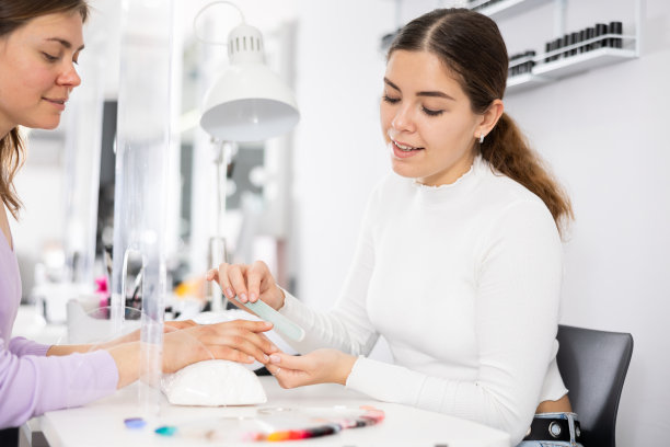 年轻女性美甲师为女性客户锉指甲和定型图片下载