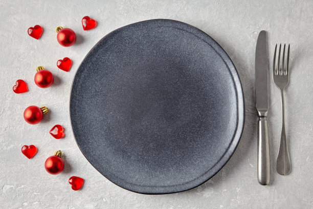 一个空的灰色陶瓷盘，上面放着餐具，周围是红色的圣诞球和爱心图片下载