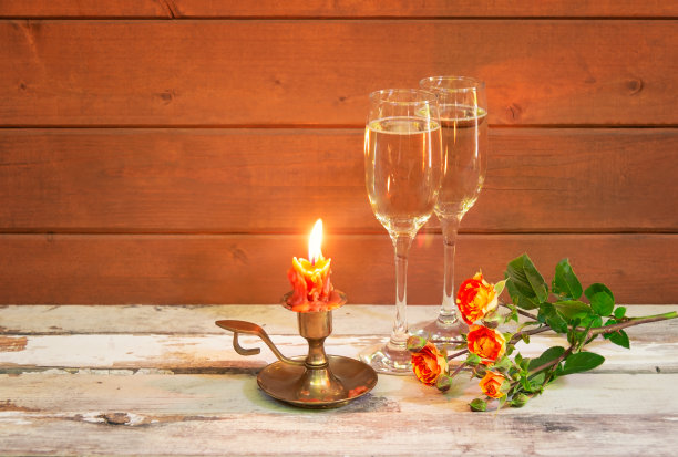 老旧的木桌上摆着燃烧的蜡烛、香槟和橙玫瑰。图片下载