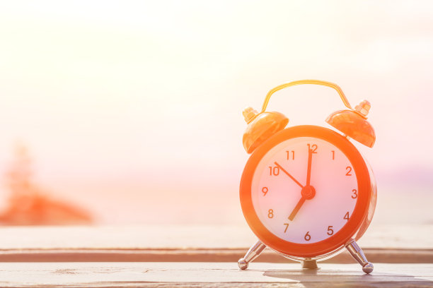 早上好，概念。红色闹钟在木桌上日出在海上的背景。本空间图片下载