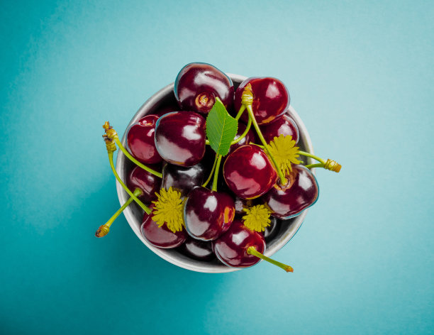 新鲜多汁的樱桃与花在碗孤立在蓝色背景的俯视图图片下载