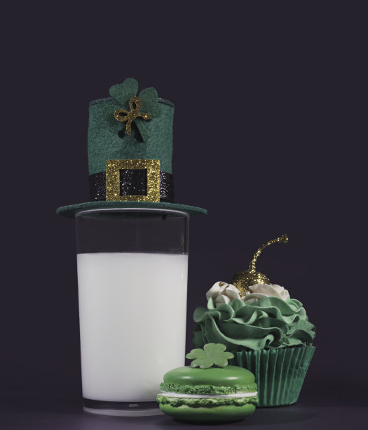 圣帕特里克节的三样早餐:一杯戴着小妖精帽子的牛奶，一块绿色马卡龙饼干，还有一个上面点缀着亮片樱桃的巧克力小蛋糕图片下载