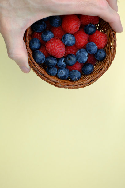 人们拿着一个小篮子，里面装满了新鲜的覆盆子和蓝莓图片下载