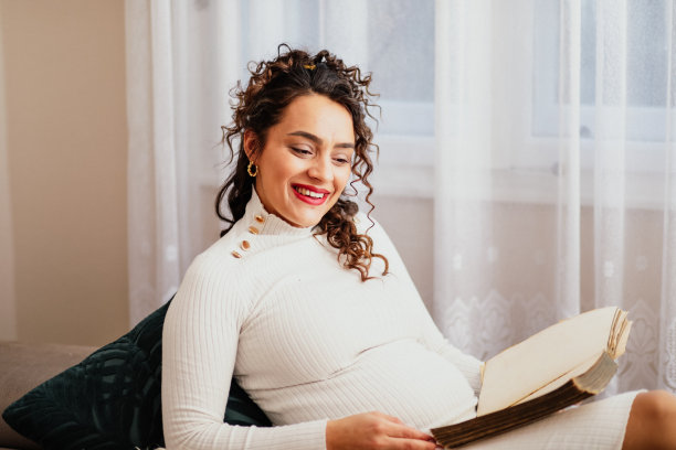 年轻的孕妇在她公寓的沙发上看书，她的宠物狗和她在一起图片下载