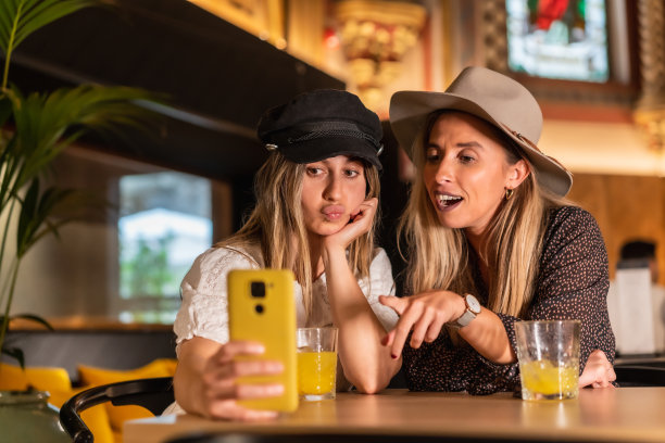 两名西班牙女子在一家现代自助餐厅的黄色沙发上喝橙汁自拍图片下载