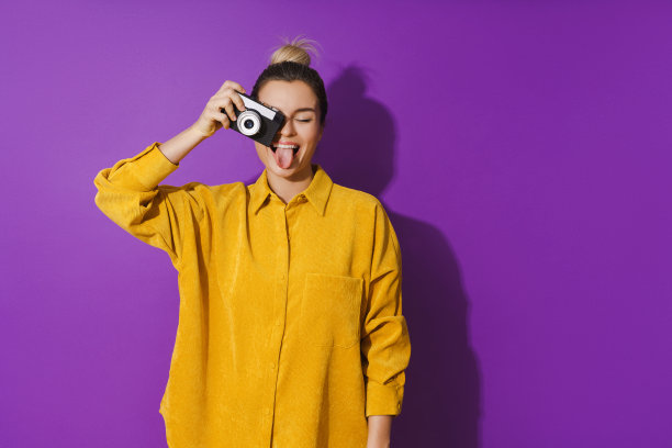 年轻开朗的女孩伸出舌头使用电影摄影相机在紫色的背景图片下载
