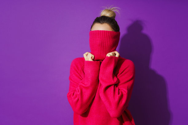 有趣的女人把她的脸藏在一件温暖舒适的polo领毛衣里，背景是紫色的图片下载