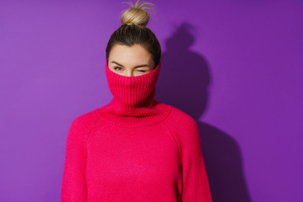 年轻女子隐藏她的脸在一件温暖舒适的polo领毛衣在紫色的背景图片下载
