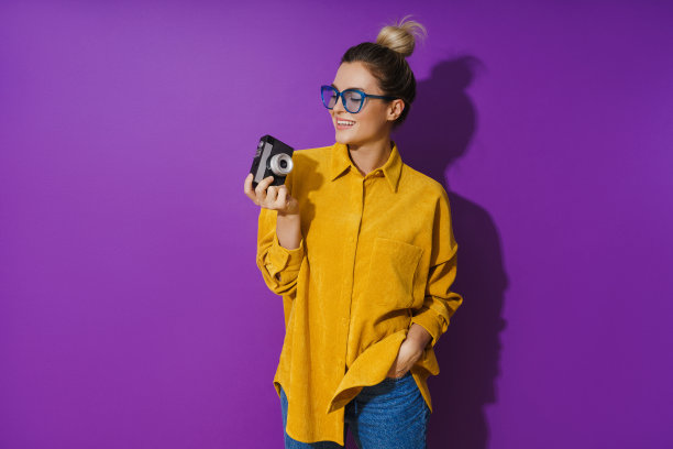 开朗的女孩戴着眼镜，拿着紫色背景的老式胶卷相机图片下载